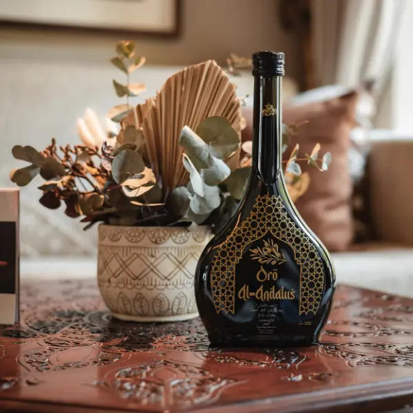 Botella de aceite de oliva virgen extra Oro Al-Andalus sobre una mesa de madera tallada en un ambiente interior con decoración elegante y floral.