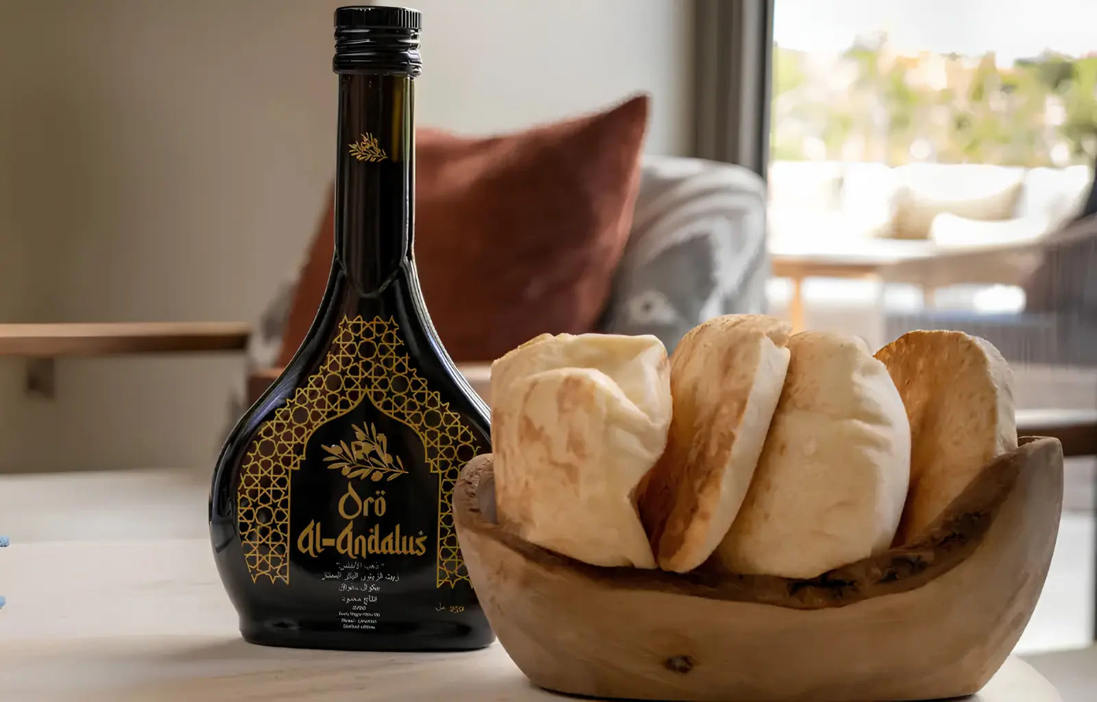 Botella Arabesca de aceite de oliva virgen extra Oro Al-Andalus junto a un cuenco de madera con pan, ideal para degustar el AOVE premium en crudo.